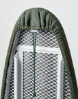 Close-up of an olive green ironing board cover fitted to a ironing board, showing the drawstring and the fabric texture.