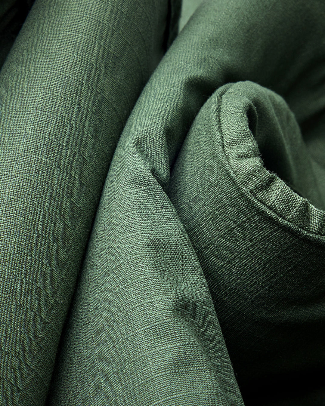 Close-up of olive green 100% cotton ripstop fabric, showing fabric weave and grid structure, folded naturally.