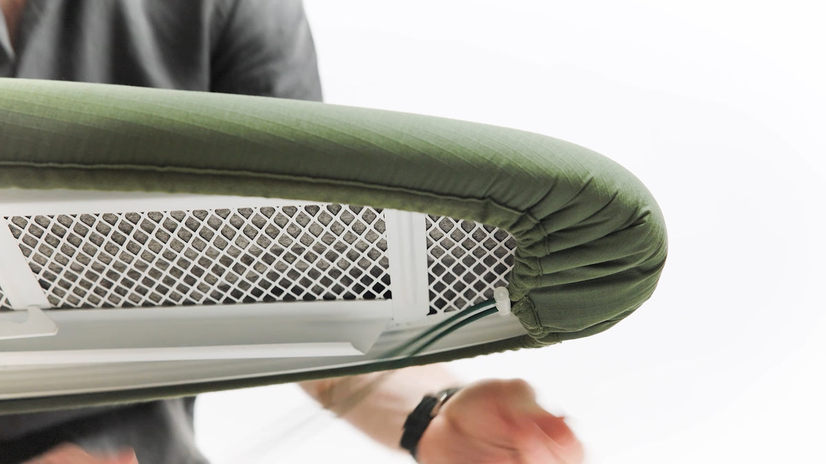 Close-up of olive green padded ironing board cover fitted to a white ironing board.