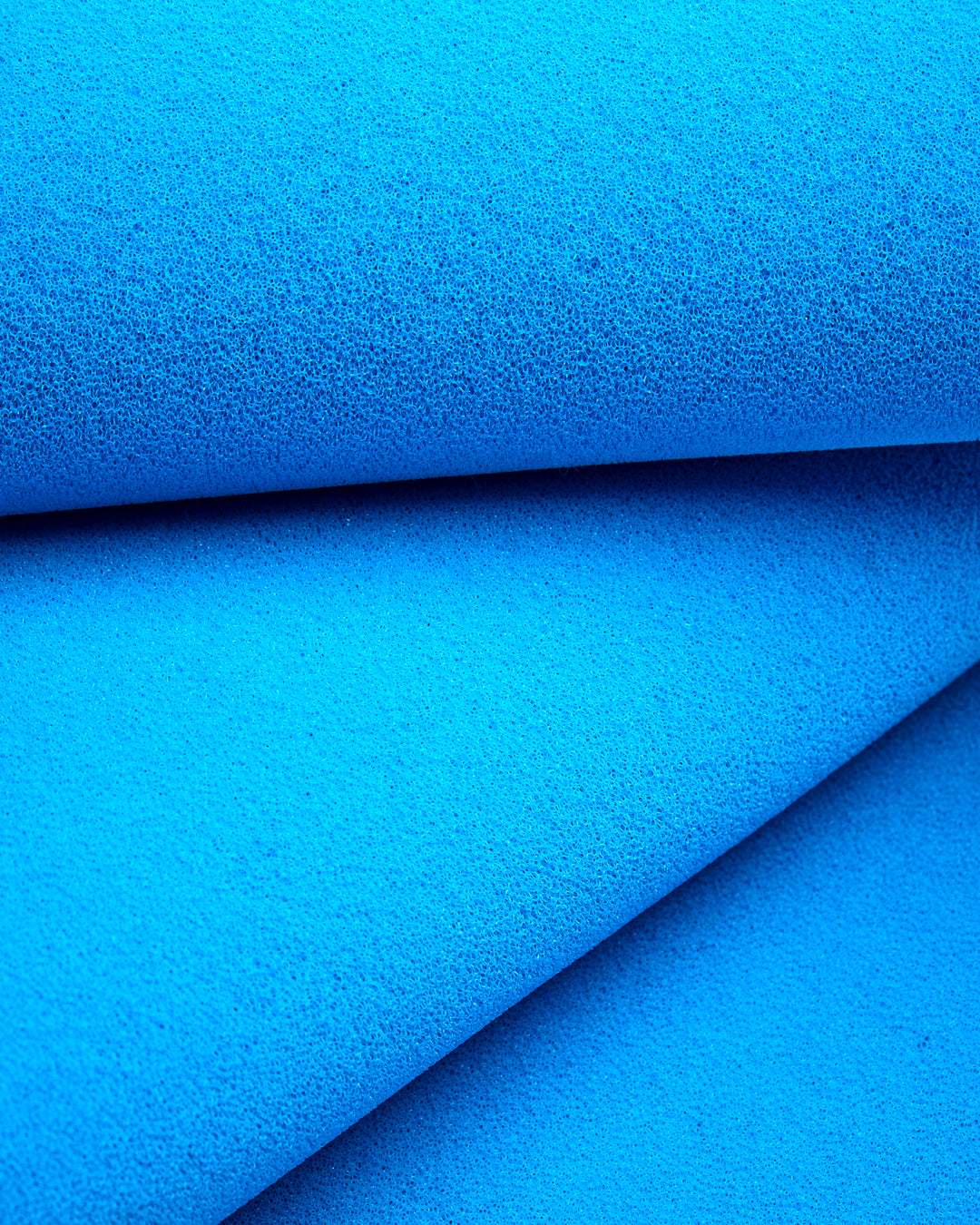 A close-up macro image of bright blue open cell silicone foam, showing the cell structure, folded across the frame.