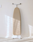 A beige ironing board cover on a white board, photographed in a modern, warm, shadow light interior.
