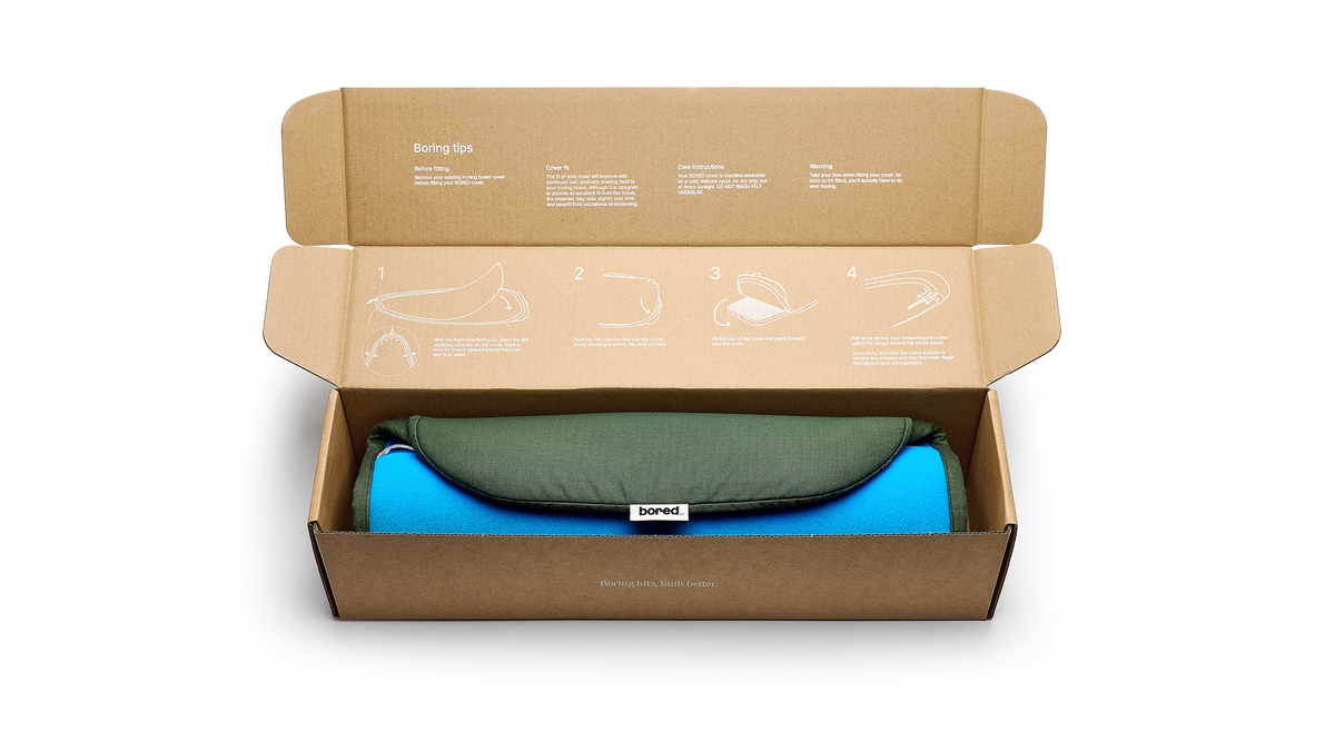 An open cardboard box containing a ironing board cover in olive green, and a "bored" branding label.